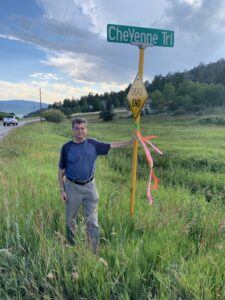 Photo: Outdoors, a man poses next to a street sign with a ribbon tied around it.